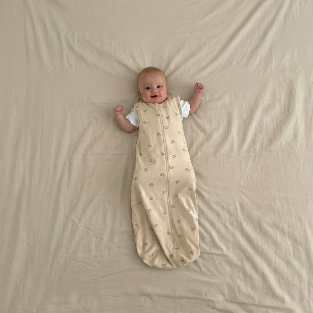 Baby lying on a beige blanket wearing a warm white sleep bag with goldilocks pattern