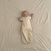 Baby lying on a beige blanket wearing a warm white sleep bag with goldilocks pattern