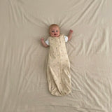 Baby lying on a beige blanket wearing a warm white sleep bag with goldilocks pattern
