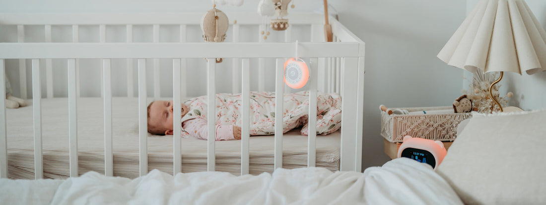 Baby sleeping in a cot with a white noise machine and Sleep Like Goldilocks bear nearby