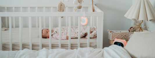 Baby sleeping in a cot with a white noise machine and Sleep Like Goldilocks bear nearby