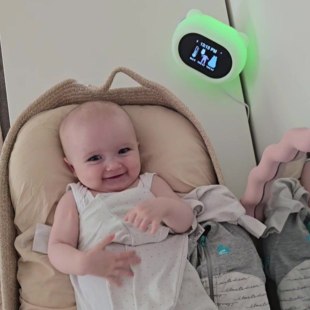 Smiling baby lying beside sleep sacks, with the Sleep Like Goldilocks thermometer showing TOG guidance on the wall