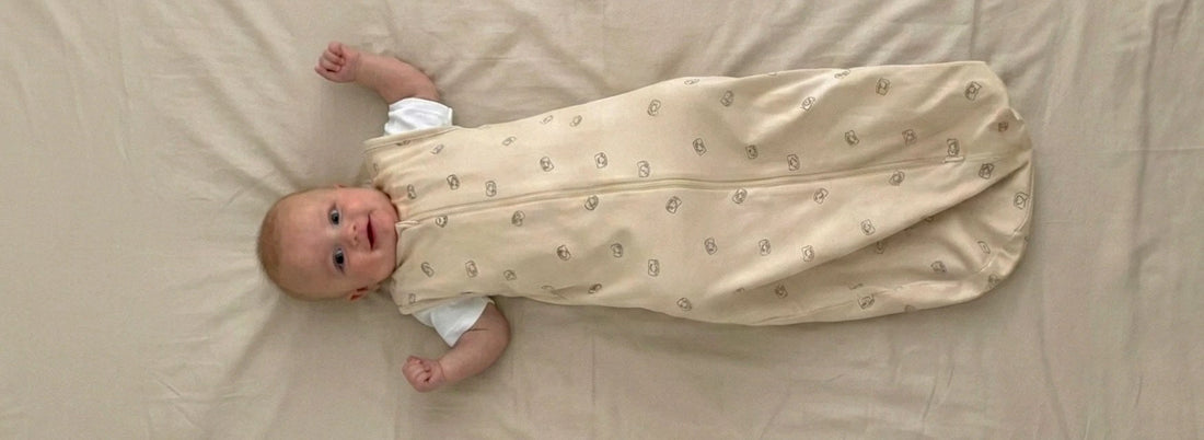 Smiling baby lying on a beige blanket in a lightweight cotton sleeping bag