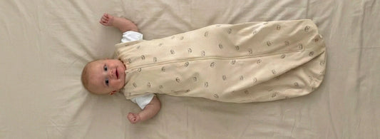 Smiling baby lying on a beige blanket in a lightweight cotton sleeping bag